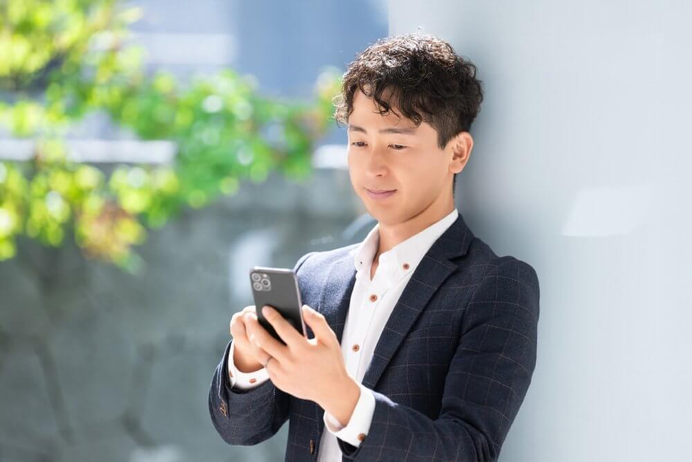 スマホを触りながら微笑むジャケット姿の男性。