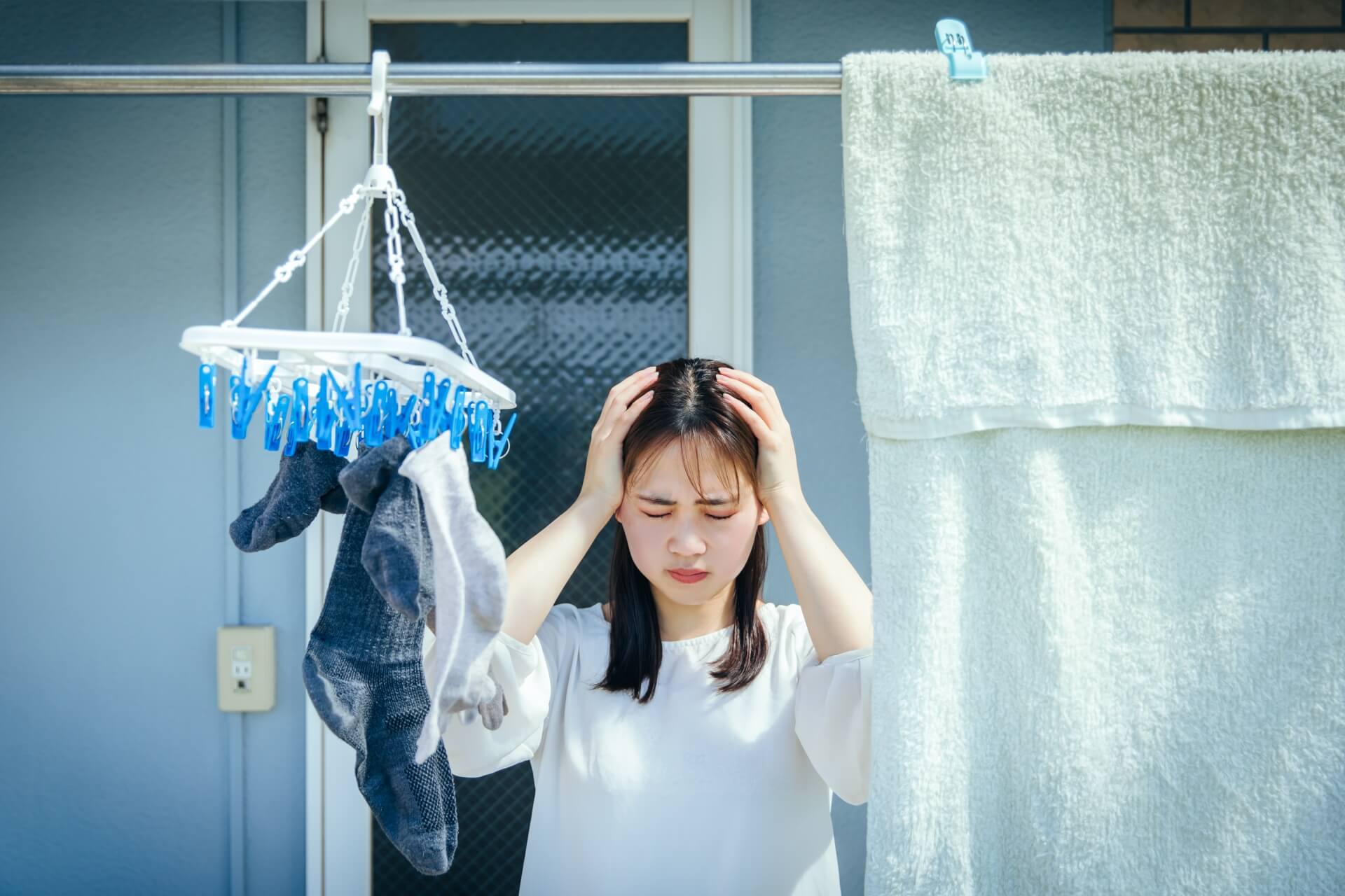 ベランダで干した洗濯ものの下で頭を抱える女性