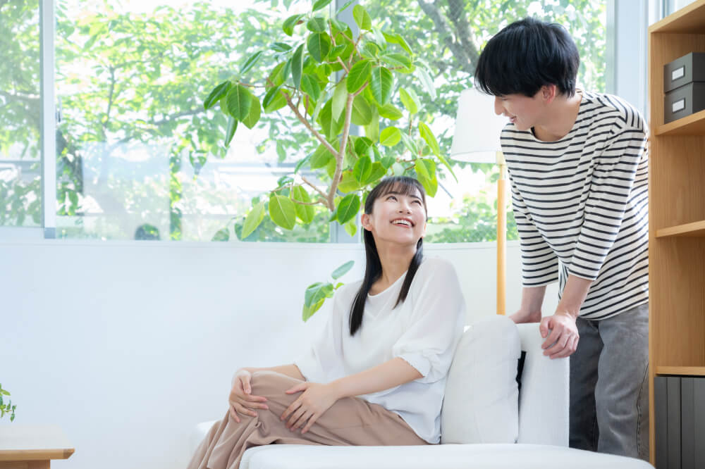 リビングのソファに座る女性とソファの後ろにいる男性。お互いに顔を見合わせて笑っている。くつろいでいる様子。