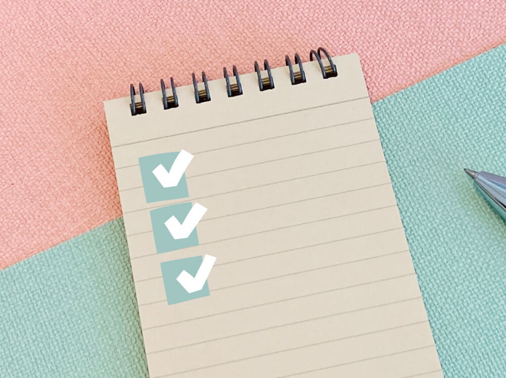 ピンクと薄いみどりの背景紙の上にメモ帳が置いてあり、チェックリストが書いてある。