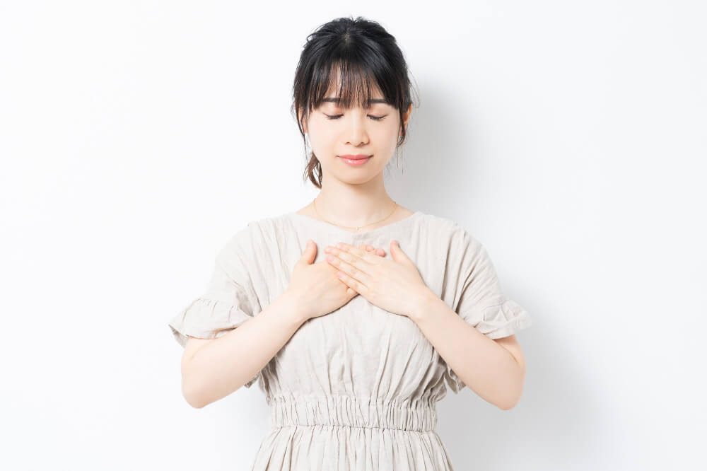 ベージュのワンピースを着た女性が目をつむり両手を胸にあてている