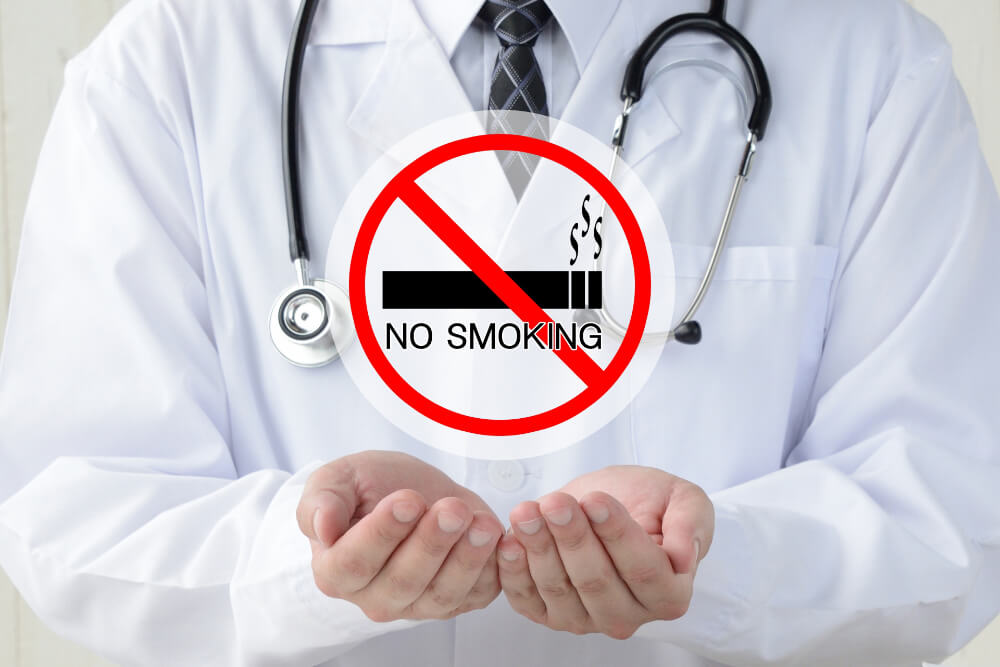 禁煙外来のイメージ 白衣の男性が首から聴診器をぶら下げており両手を前に出している。両手の上には、「No Smoking」の文字が載った禁煙のロゴマーク。