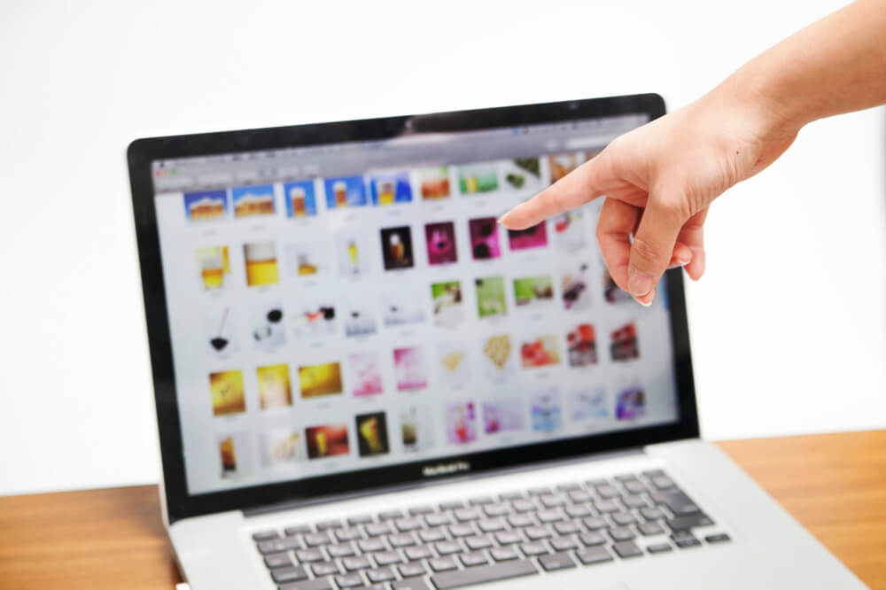 ノートパソコンにひらかれた写真一覧とそれを指さす手