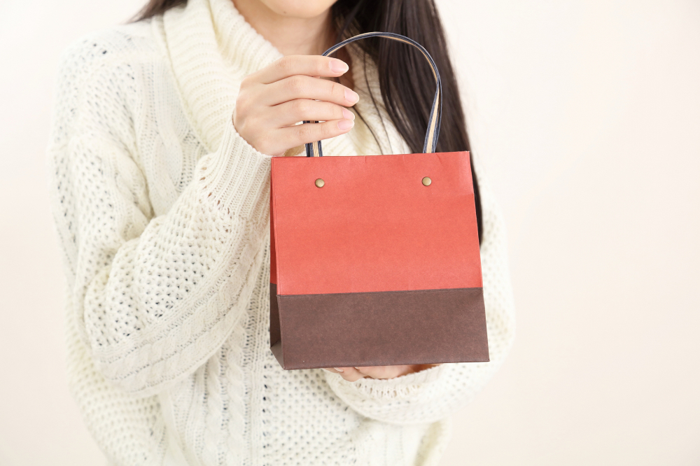 オレンジと茶色のツートンカラーの紙袋を持つ女性。白いニットを着ている