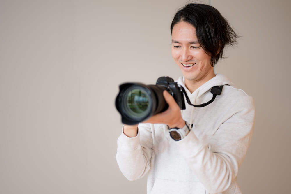 生成りのフードパーカーを来た男性が、一眼レフカメラを持って操作している