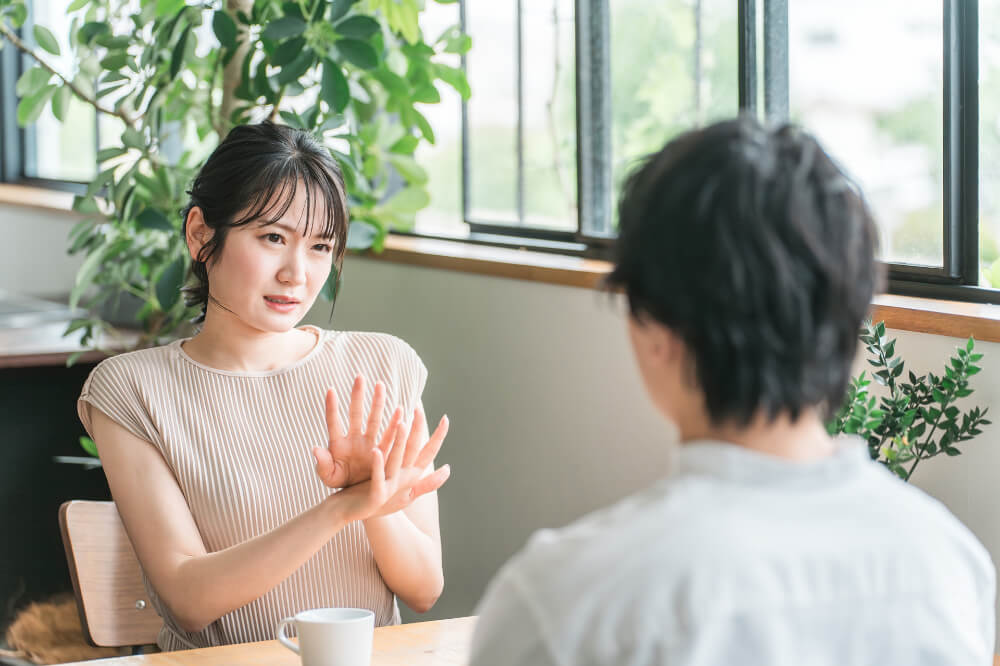 拒否反応を示す女性 カフェの窓際の席に向き合って座る男女。男性は後ろ姿。女性は、腕をクロスして険しい表情で男性に対して拒否反応を示している