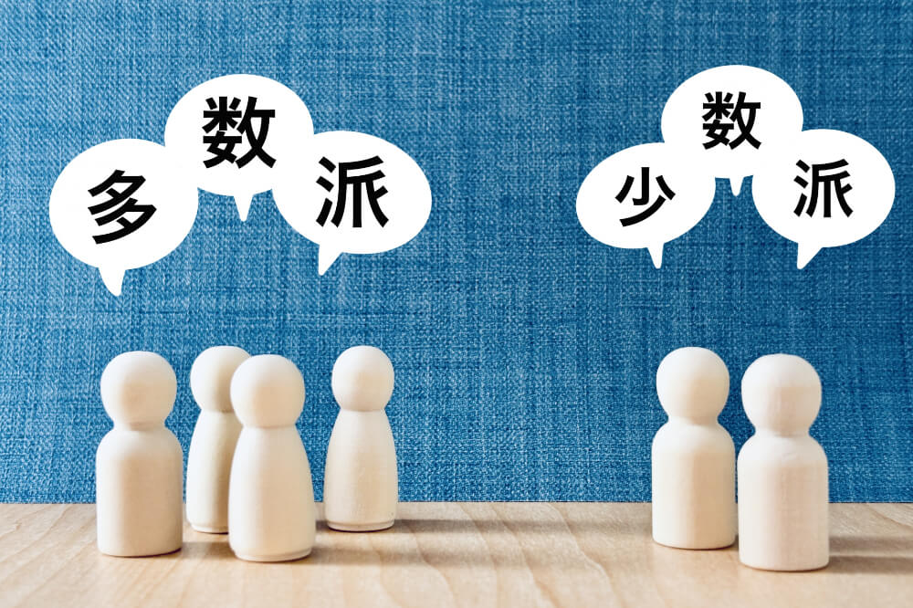 デニム生地の背景で、手前に気の人形がいくつか置いてある。左には４つ、多数派という吹き出し付。右側には２つ、少数派という吹き出しが付いている